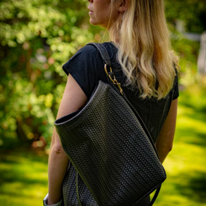 Person wearing a dark woven backpack outdoors with greenery in the background
