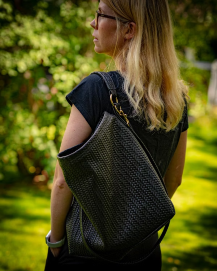 Person wearing a dark woven backpack outdoors with greenery in the background